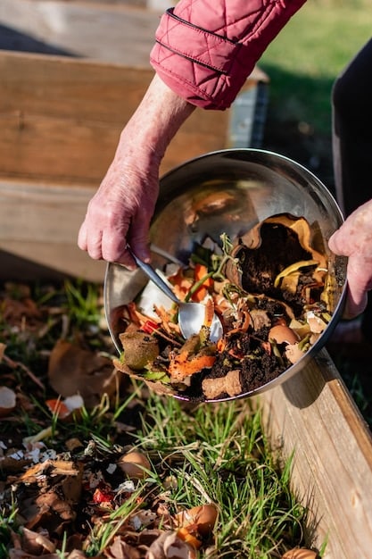 A person's hands carefully mixing compost in a garden setting. The compost bin is overflowing with vegetable scraps, leaves, and coffee grounds, showcasing the recycling of organic waste.