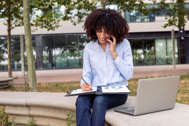 A person on a phone call, looking determined and holding a pen ready to take notes, with a stack of papers and a laptop in front of them, suggesting an active negotiation.