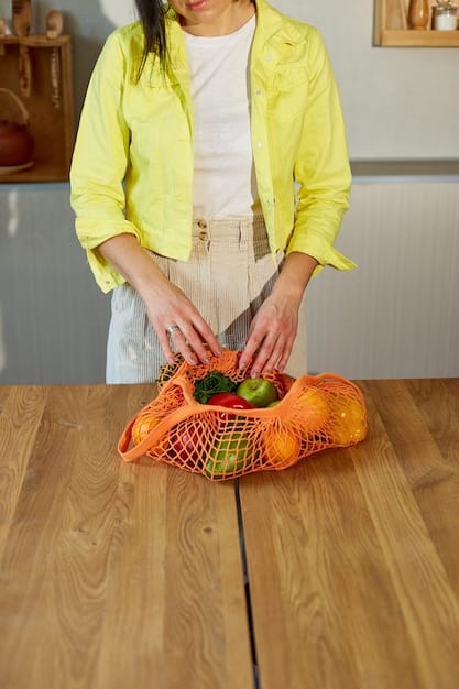 Close-up of hands organizing colorful fresh vegetables like bell peppers, zucchini, and carrots into reusable mesh bags inside a modern refrigerator, showcasing organized food storage.