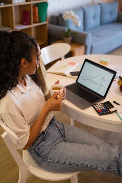 A person looking thoughtfully at a financial calculator on their laptop, with various charts and graphs representing income and expenses in the background, suggesting careful financial planning.