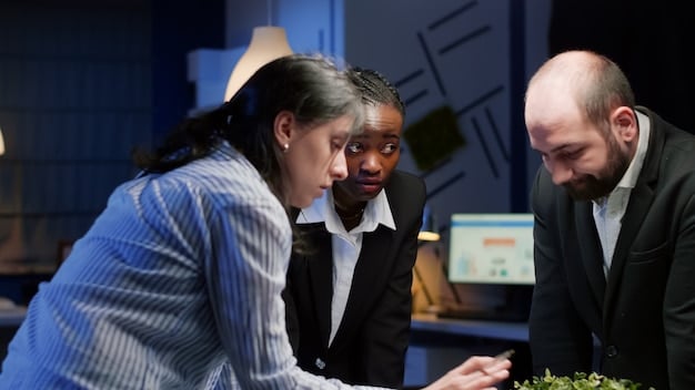 A diverse group of business professionals in a modern office looking at graphs and a large screen, engaged in a discussion about cybersecurity strategy, showing collaboration and awareness.