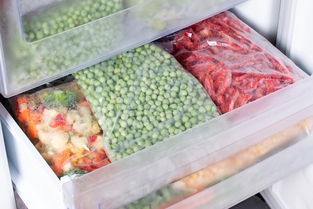 An open freezer, well-organized with clear plastic bins and labeled freezer bags. The bins are categorized with labels like 