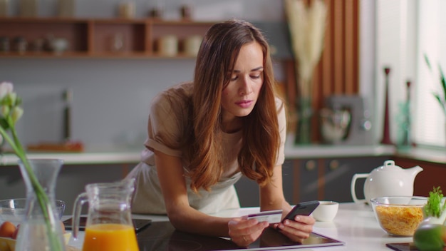 A person using a budgeting app on their smartphone while sitting at a kitchen table. The app displays a detailed breakdown of grocery expenses, categorized by food type. The kitchen has a calendar on the wall with meal plans written. This scene emphasizes the tech and process involved in a 'Grocery Budget Reset: How to Cut Spending by 15% in 30 Days'.